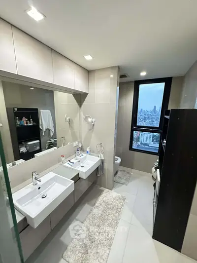 Modern bathroom with dual sinks and city view from window, featuring sleek design and ample storage.