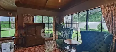 Luxurious living room with elegant furniture and garden view, featuring large windows and plush seating.