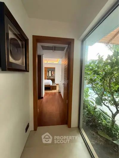 Stylish hallway leading to a cozy bedroom with wooden flooring and large window view.