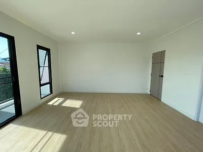 Spacious empty room with wooden flooring and large windows offering natural light.