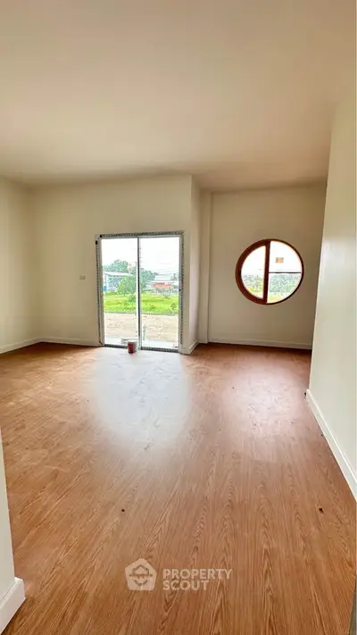 Spacious living room with unique round window and wooden flooring, offering a bright and airy atmosphere.