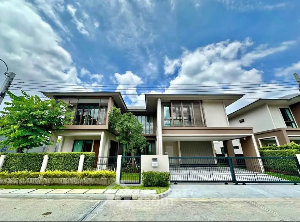 Modern two-story house with lush garden and spacious driveway under a clear blue sky.