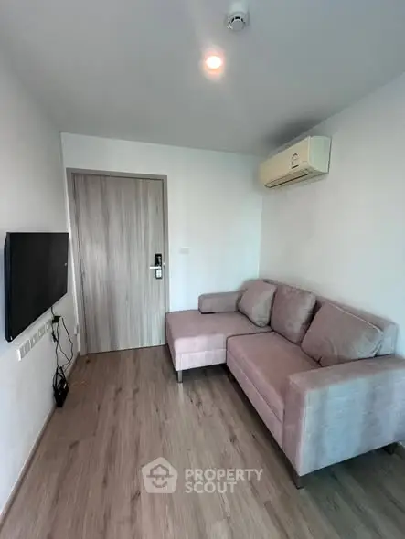 Modern living room with sleek wooden flooring and cozy L-shaped sofa, featuring a wall-mounted TV and air conditioning.