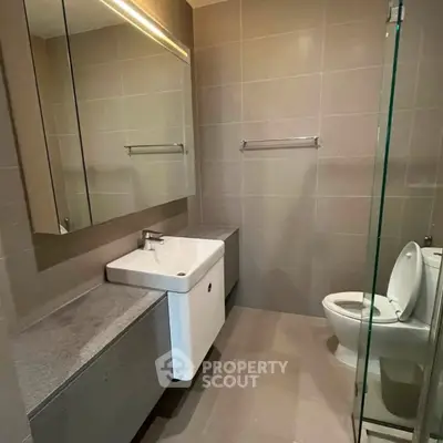 Modern bathroom with sleek design, featuring a large mirror, glass shower, and contemporary fixtures.