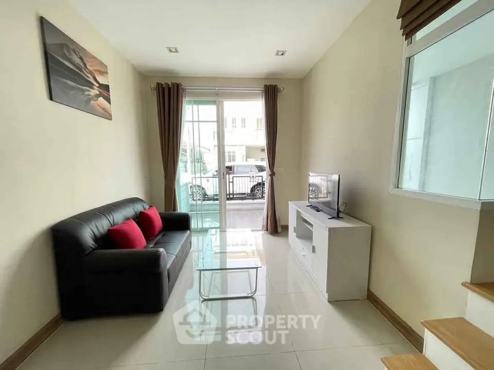 Cozy living room with modern decor and natural light, featuring a sleek black sofa and TV setup.