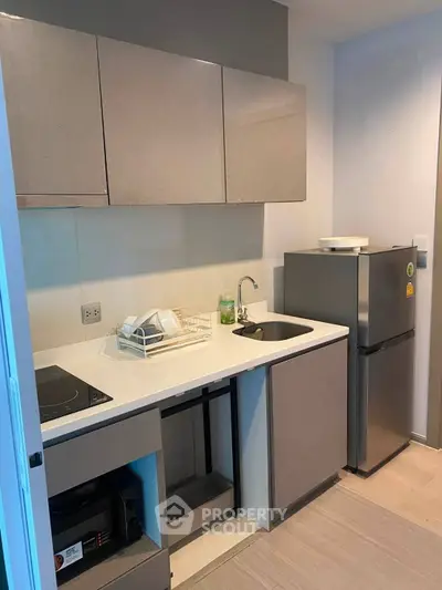 Modern compact kitchen with sleek cabinetry and stainless steel fridge in a stylish apartment.