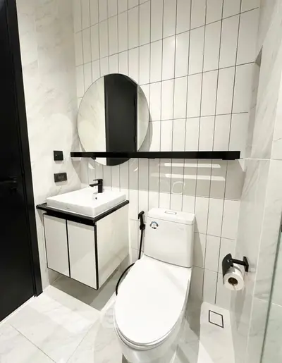 Modern bathroom with sleek white tiles and minimalist fixtures, featuring a round mirror and compact vanity.