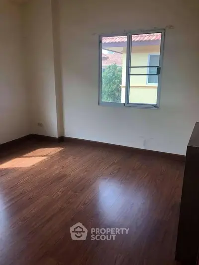 Spacious empty room with wooden flooring and a window view, perfect for customization.