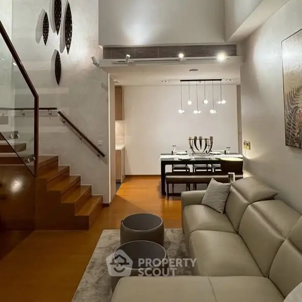 Modern living room with elegant staircase and dining area, featuring stylish lighting and decor.