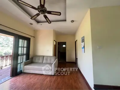 Spacious living room with wooden floors and ceiling fan, opening to a balcony with scenic views.