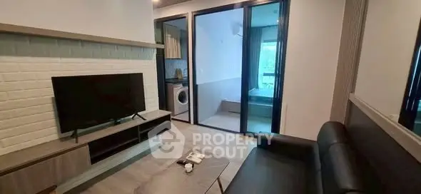 Modern living room with TV, black sofa, and view into bedroom and kitchen with washing machine.