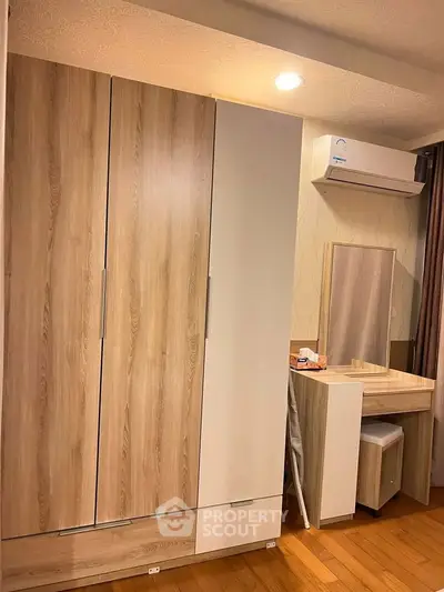 Modern bedroom with stylish wardrobe and vanity, featuring wooden flooring and air conditioning.