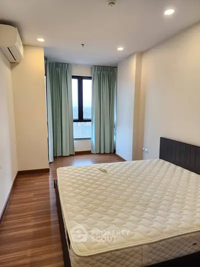 Spacious bedroom with large window and modern furnishings in a stylish apartment.