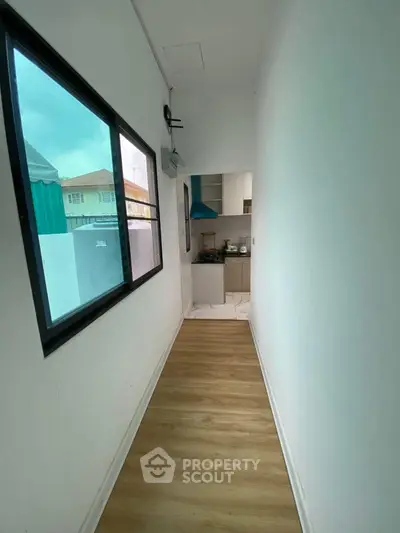 Narrow hallway leading to a compact kitchen with modern appliances and wooden flooring.