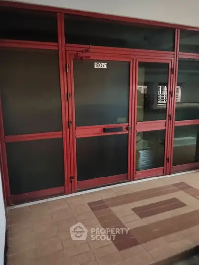 Red-framed glass entrance with tiled flooring in a residential building.