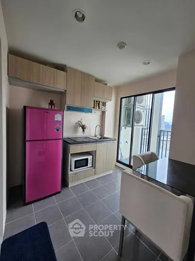 Modern kitchen with vibrant pink fridge and sleek cabinetry in a high-rise apartment with city view.