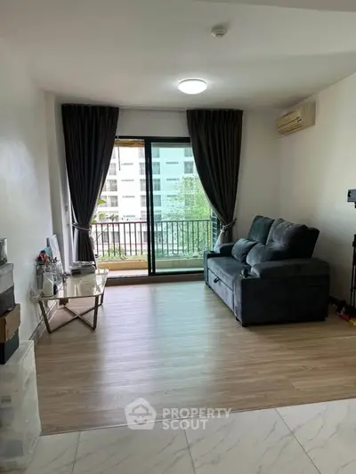 Spacious living room with modern decor and large window offering natural light and balcony access.