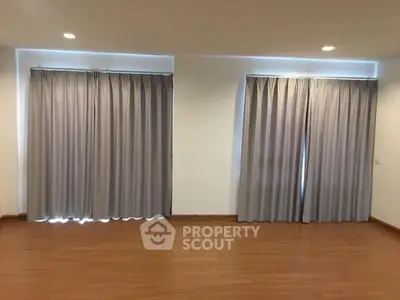 Spacious room with wooden flooring and large windows covered by elegant curtains.