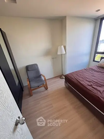 Cozy bedroom with wooden flooring, large window, and modern furniture in a stylish apartment.