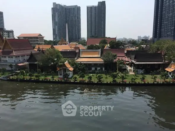 Scenic riverside view with lush gardens and modern high-rise buildings in the background.