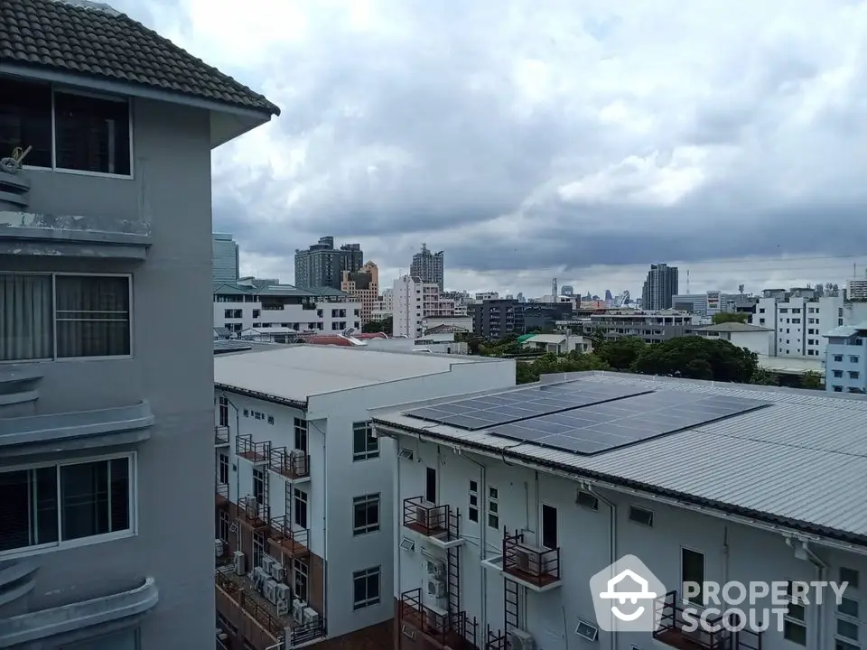 Cityscape view from apartment balcony with solar panels and cloudy sky