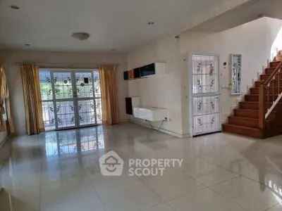 Spacious living room with elegant staircase and large windows, perfect for natural light and modern living.