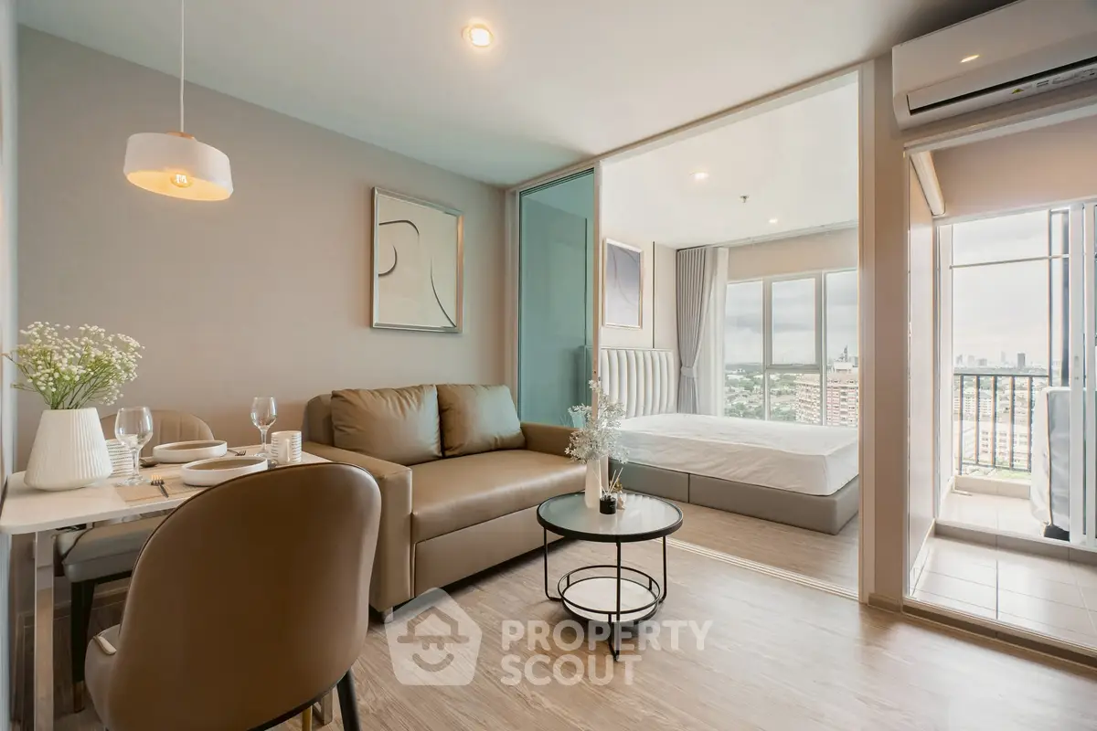 Modern open-plan living room with dining area and bedroom, featuring a balcony with city views.