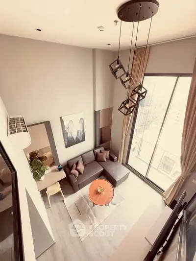 Modern living room with high ceiling and large windows offering city views.