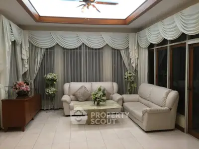 Elegant living room with plush sofas and floral decor, featuring large windows and ceiling fan.