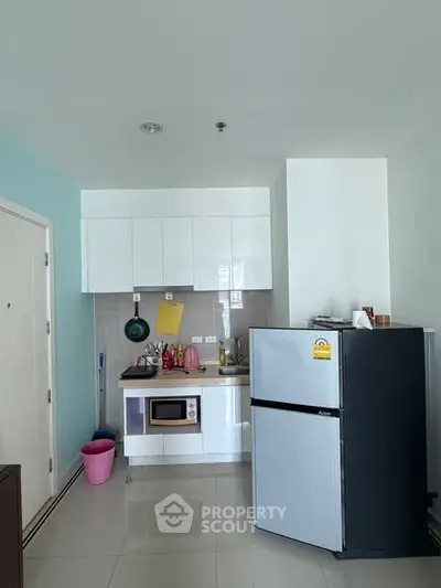 Modern compact kitchen with sleek white cabinets and stainless steel fridge in a cozy apartment.