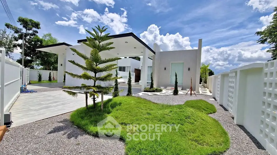 Modern white villa with lush green landscaping and clear blue sky, showcasing contemporary architecture.