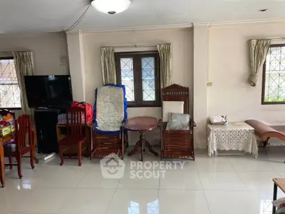 Spacious living room with tiled flooring and natural light, featuring wooden furniture and a TV setup.