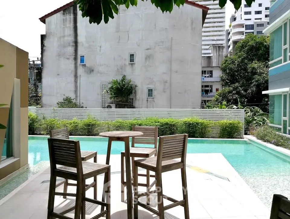 Charming poolside area with wooden furniture and urban backdrop, perfect for relaxation.