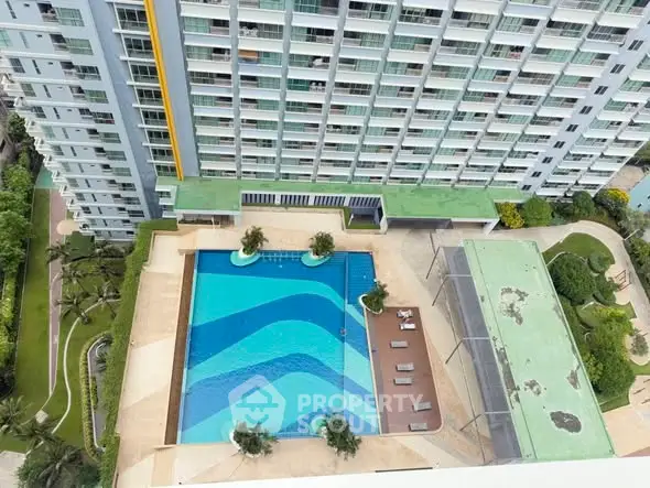 Aerial view of modern condominium with large swimming pool and lush garden.