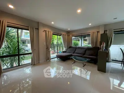 Spacious living room with modern sofa and large windows overlooking lush greenery.