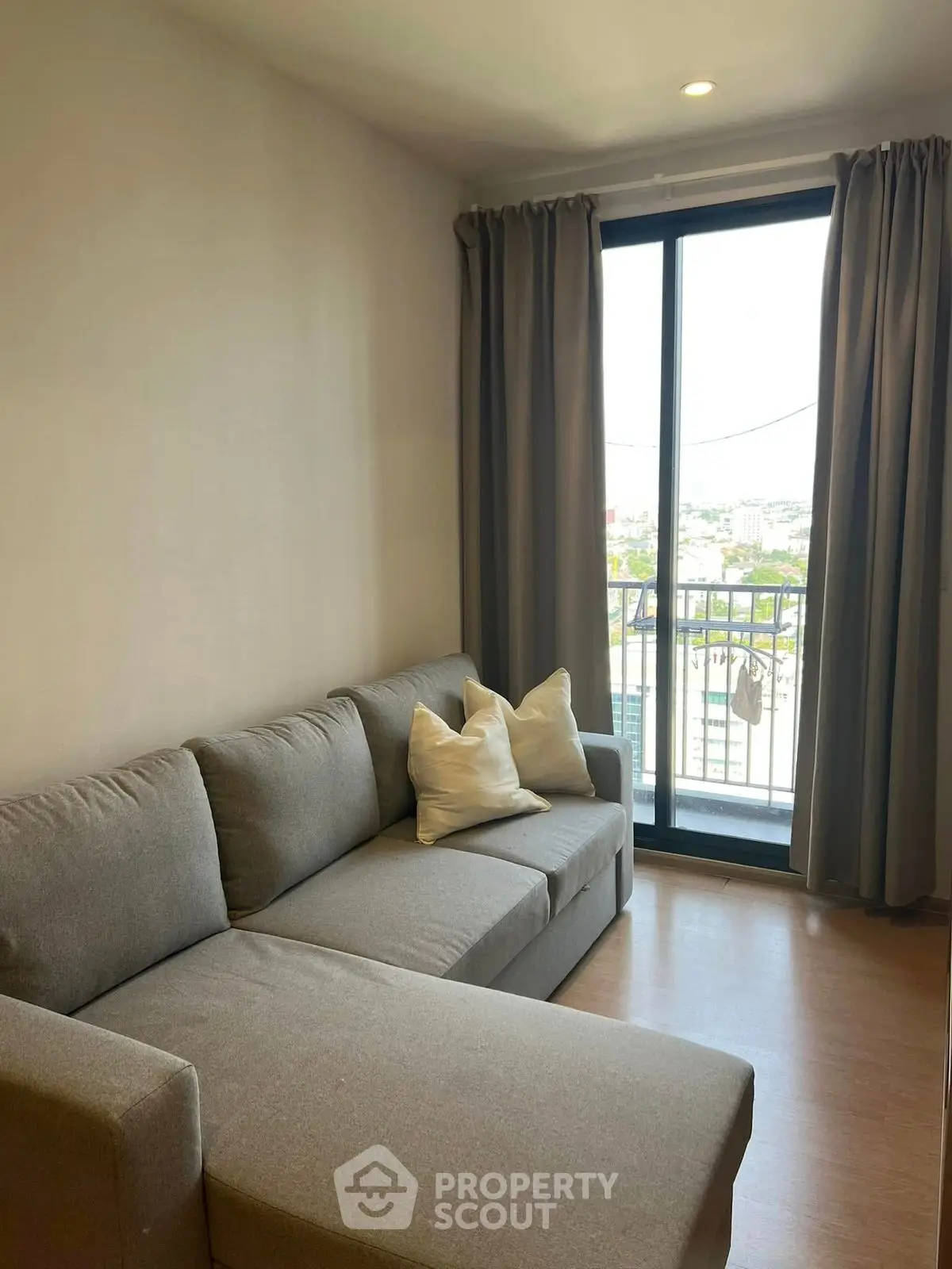 Cozy living room with gray sofa and city view from balcony.