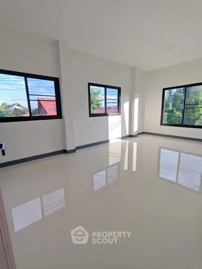 Spacious sunlit room with large windows and glossy tiled floors, perfect for versatile living space.