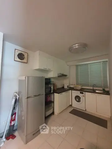 Modern kitchen with appliances including fridge and washing machine, sleek cabinetry, and tiled flooring.