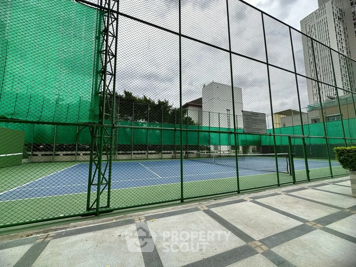 Spacious outdoor tennis court in modern urban setting with high-rise buildings.