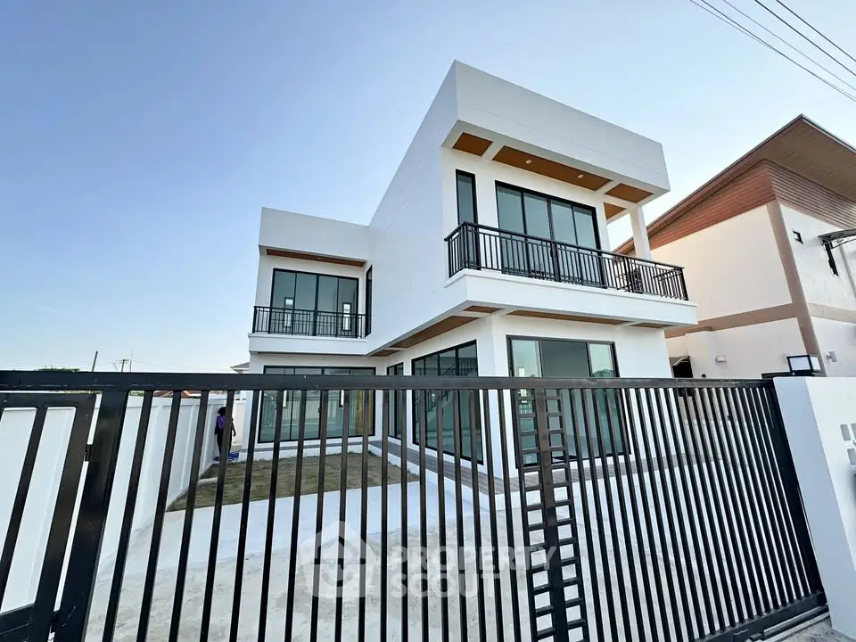 Modern two-story house with large windows and balcony, featuring sleek design and spacious outdoor area.