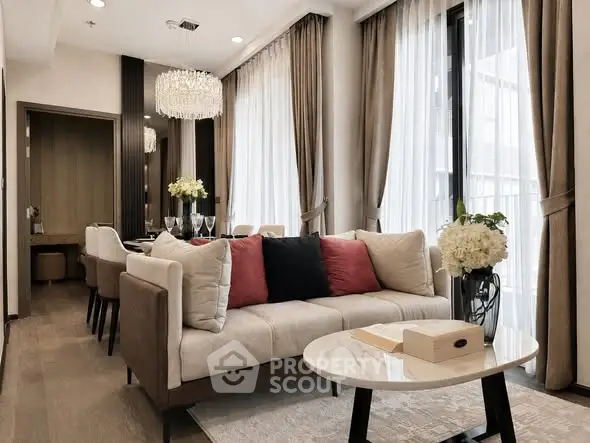Elegant living room with modern decor and dining area, featuring plush sofa and stylish chandelier.
