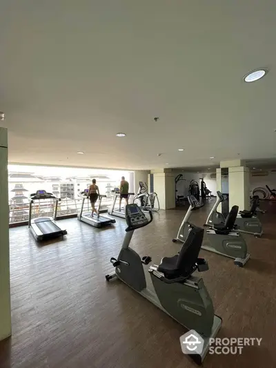 Spacious gym with modern equipment and city view in luxury apartment complex.