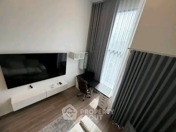Modern living room with large TV, sleek desk, and floor-to-ceiling curtains.