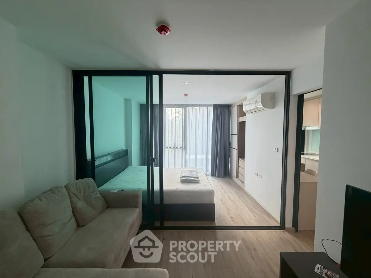 Modern studio apartment with glass partition, cozy sofa, and natural light.