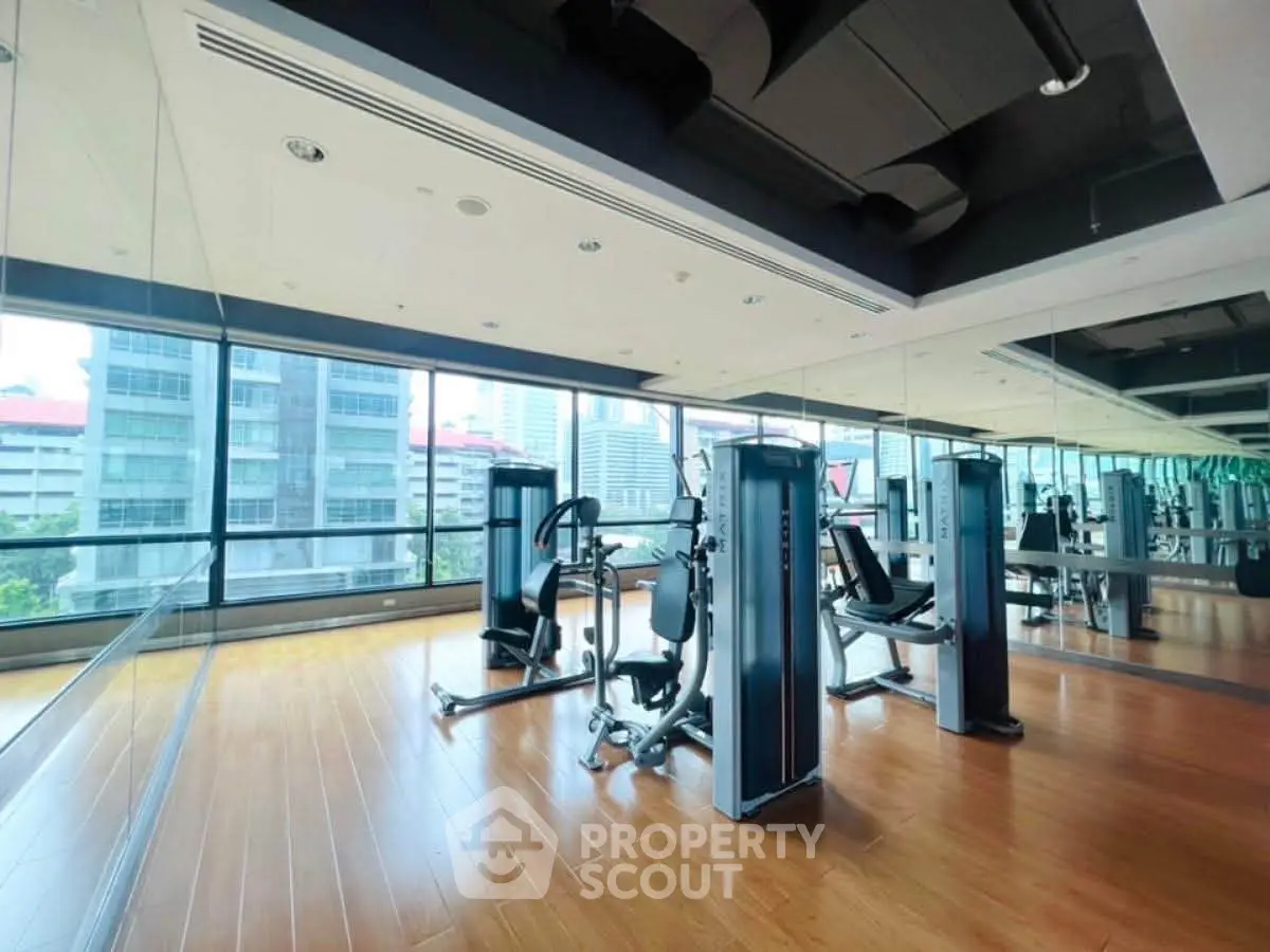 Spacious modern gym with city view and mirrored walls in luxury building.