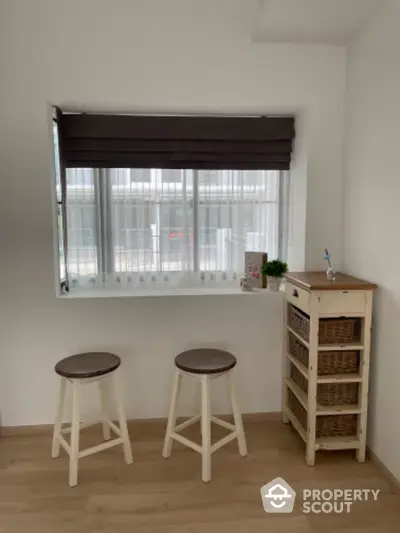 Bright and airy minimalist kitchen space with natural light streaming through a large window, complemented by modern wooden stools and storage unit.