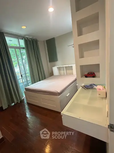 Spacious bedroom with modern design and large window overlooking greenery, featuring built-in storage and hardwood floors.