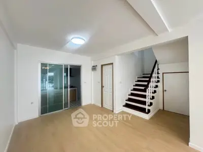Spacious living room with modern staircase and sliding glass doors in a bright, minimalist home.