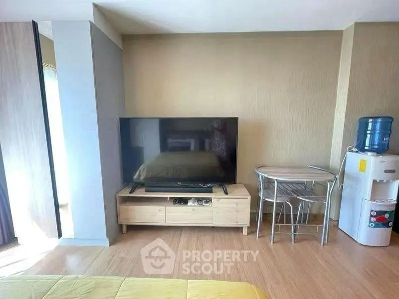 Modern living room with TV, small dining set, and water dispenser on wooden flooring.