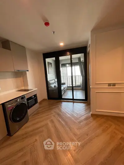 Modern apartment with sleek kitchen and washing machine, featuring herringbone wood flooring and glass doors.